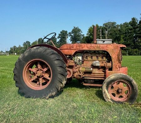 Rostig, gammal traktor på en gräsplätt under blå himmel.
