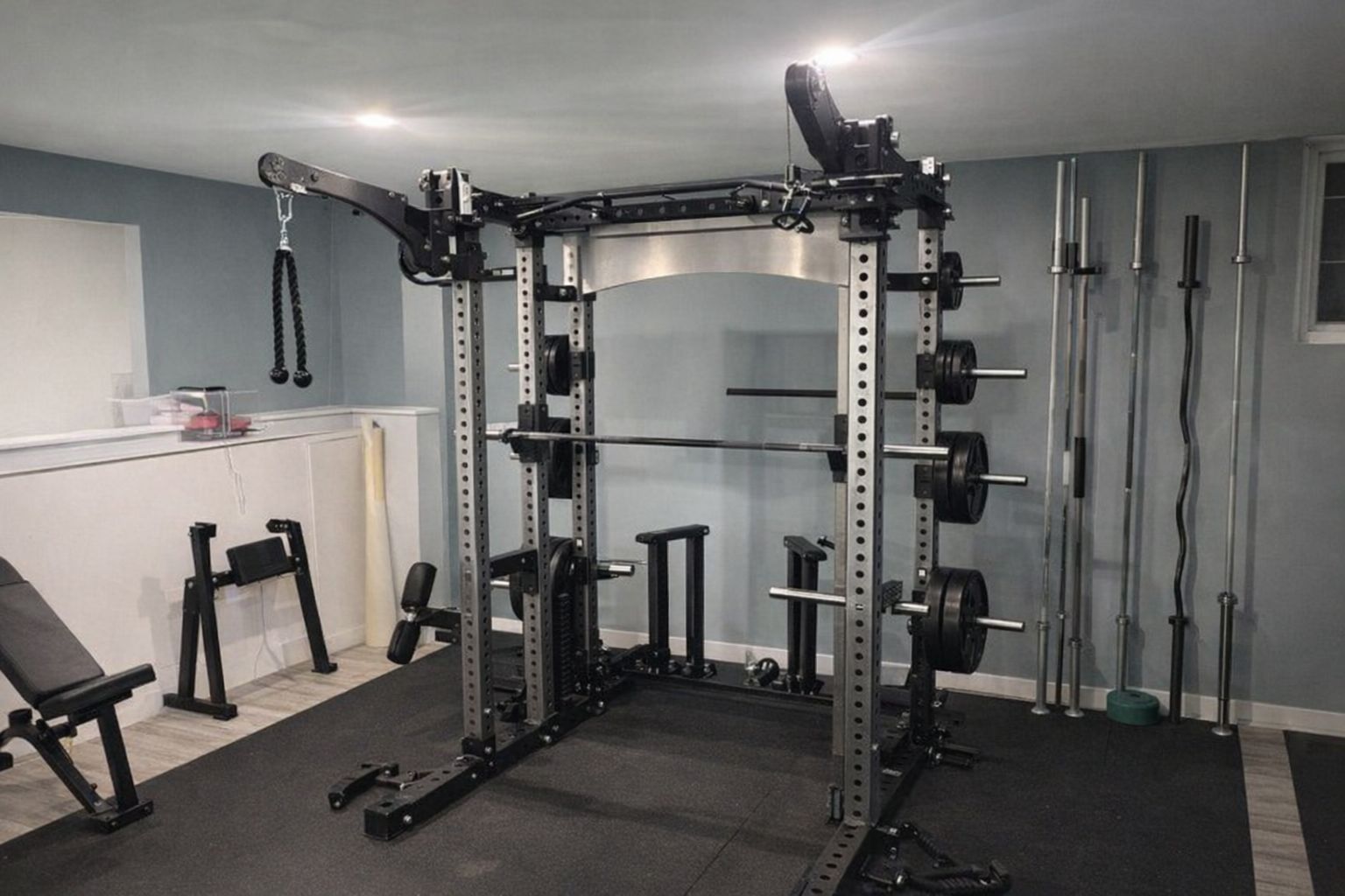 En robust skivstångsställning och multirack i ett välutrustat hemmagym.